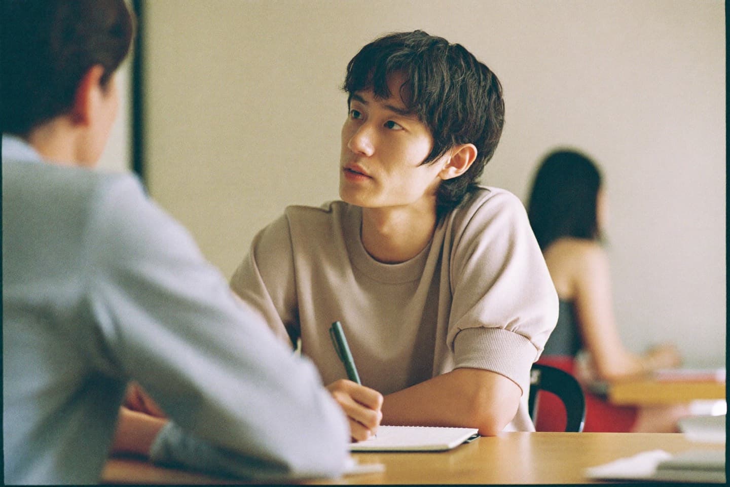 A young professional taking notes at a shared work table, listening attentively.